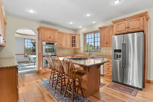 a kitchen with stainless steel appliances granite countertop a refrigerator a sink dishwasher a stove and a dining table with wooden floor