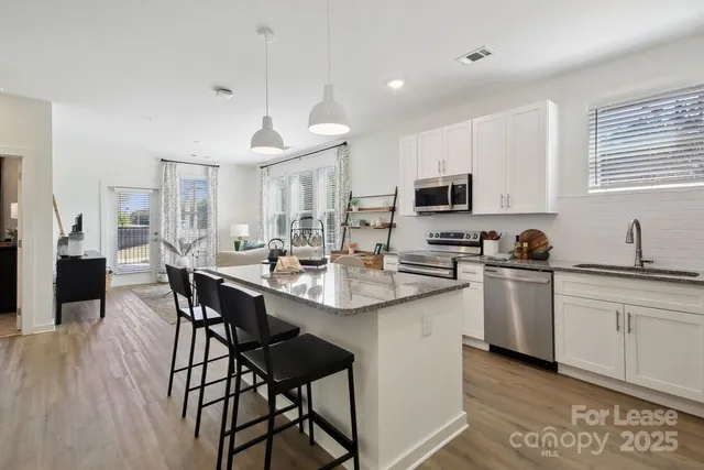 a kitchen with stainless steel appliances kitchen island granite countertop a dining table chairs and a refrigerator