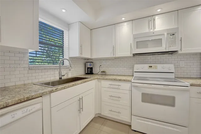 a kitchen with granite countertop white cabinets white stainless steel appliances and a sink