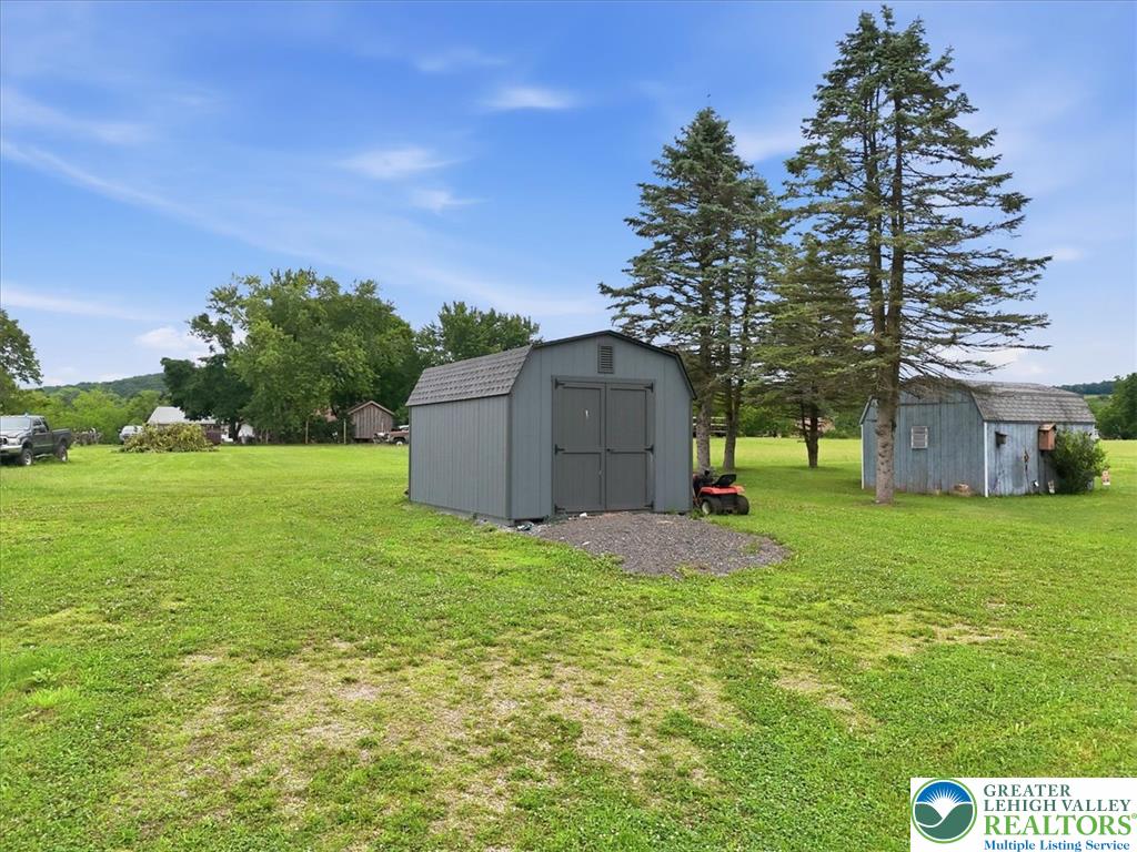 634 Main Road Lehighton, PA 18235 - Photo 34 of 39 Two utilitarian sheds sit on a vibrant green lawn under a clear, bright sky.