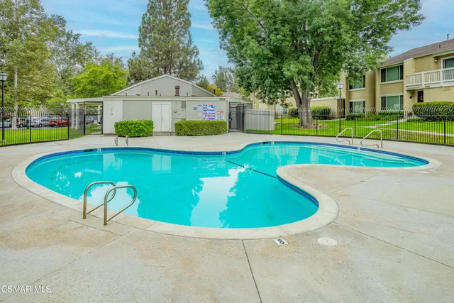 a view of a swimming pool with a bench and trees in the background