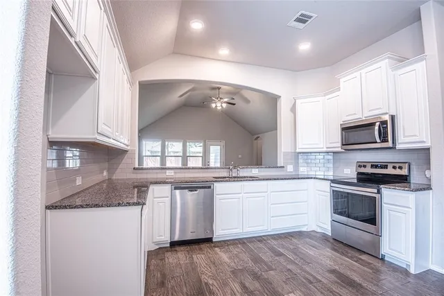 a large white kitchen with stainless steel appliances granite countertop a stove and a sink