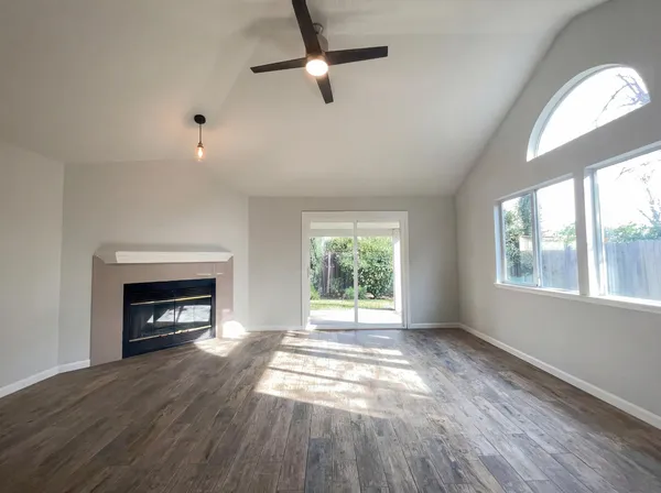 an empty room with wooden floor fireplace and windows