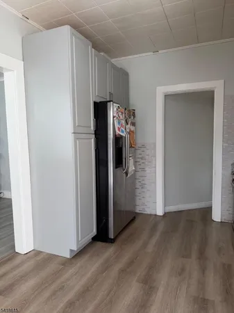 a view of a refrigerator in kitchen and an empty room with wooden floor windows