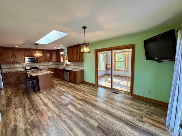 a kitchen with stainless steel appliances granite countertop a stove top oven a sink dishwasher a dining table and chairs with wooden floor