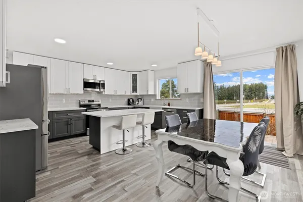 a open kitchen with stainless steel appliances granite countertop a stove a refrigerator a kitchen island a dining table and chairs with wooden floor