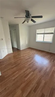 an empty room with wooden floor fan and windows