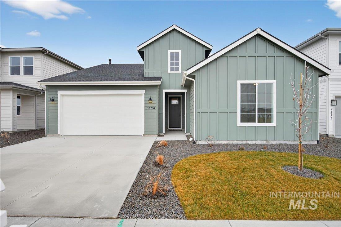 View of front facade featuring board and batten siding, concrete driveway, a garage, a front yard, and roof with shingles