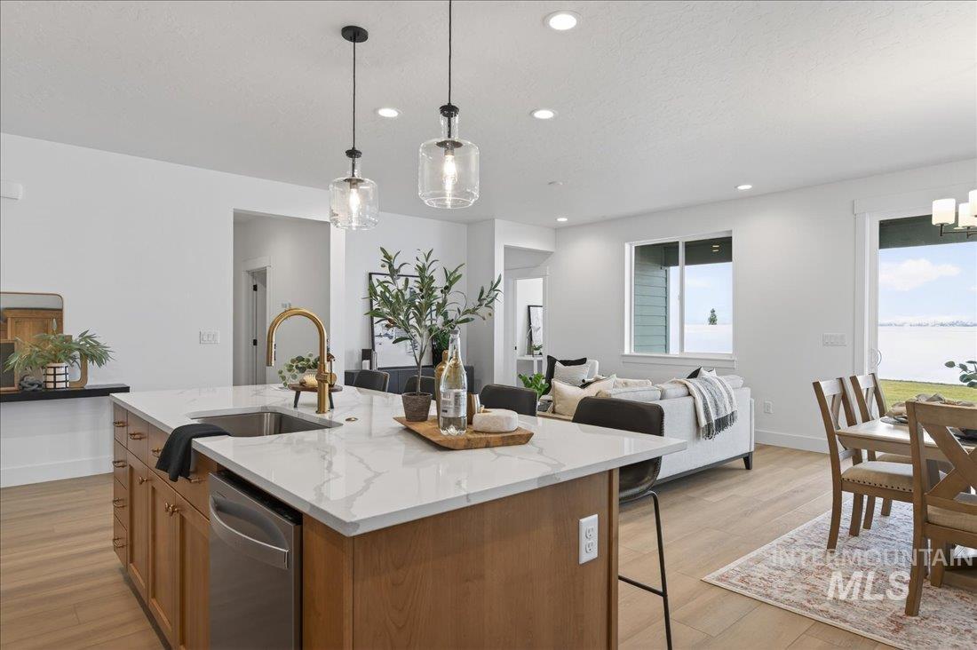 1268 West Swift Fox Street Meridian, ID 83642 - Photo 6 of 34 Kitchen featuring brown cabinetry, pendant lighting, light stone counters, a chandelier, and stainless steel dishwasher