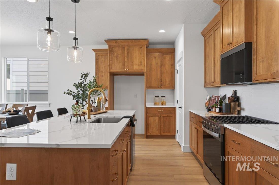 1268 West Swift Fox Street Meridian, ID 83642 - Photo 7 of 34 Kitchen with brown cabinetry, gas stove, pendant lighting, black microwave, and light wood-style floors