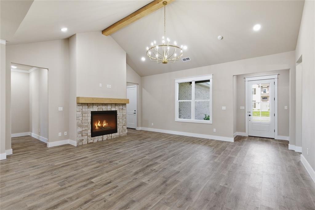 709 Anne Road Van Alstyne, TX 75495 - Photo 5 of 28 Open-concept living space featuring a stone-surround fireplace with a wood mantle, vaulted ceiling with a wood beam, and a contemporary chandelier