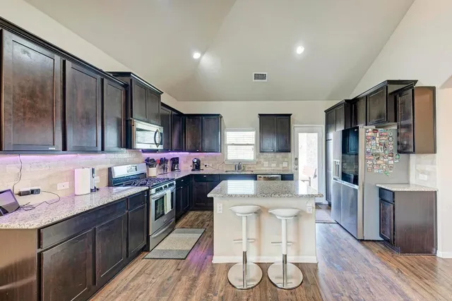 a kitchen with stainless steel appliances kitchen island granite countertop a stove refrigerator and cabinets