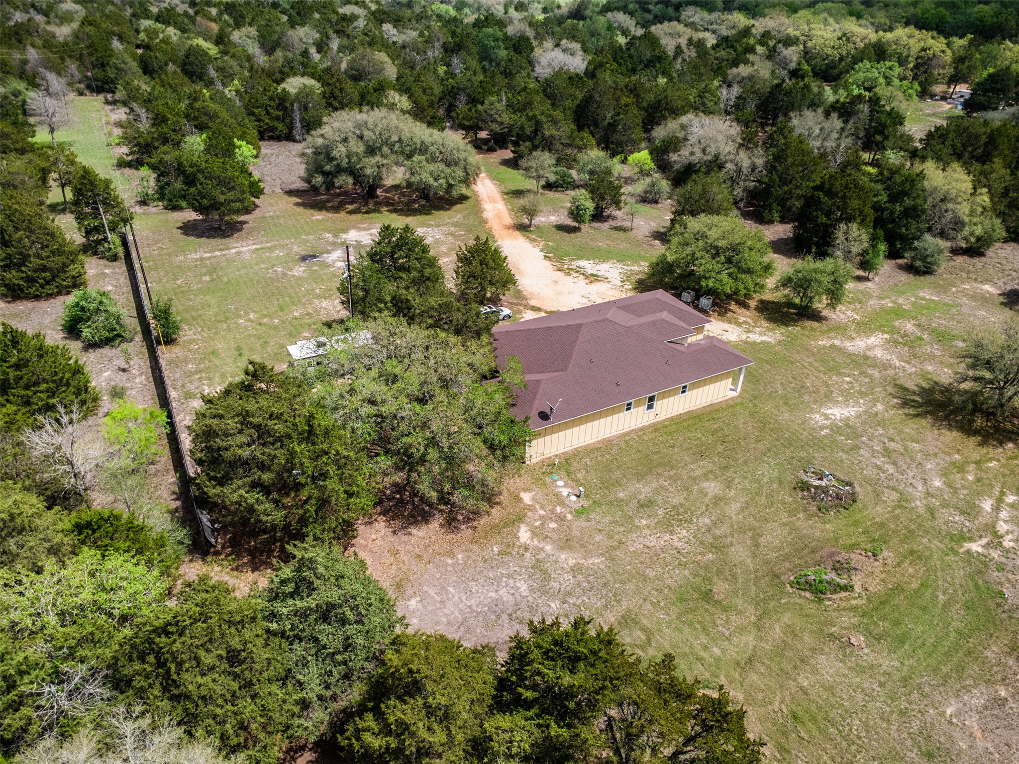 1354 Old Pin Oak Road Paige, TX 78659 - Photo 34 of 37 This property features a single-story building with a brown roof and light-colored siding, situated on a substantial lot with a dirt driveway