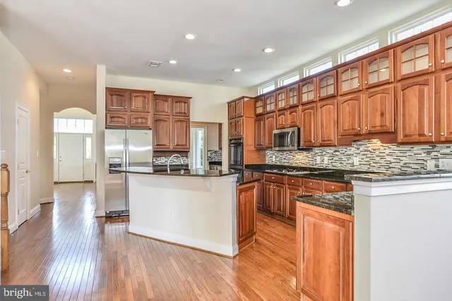 a kitchen with stainless steel appliances granite countertop wooden cabinets a refrigerator a stove a sink and dishwasher with wooden floor