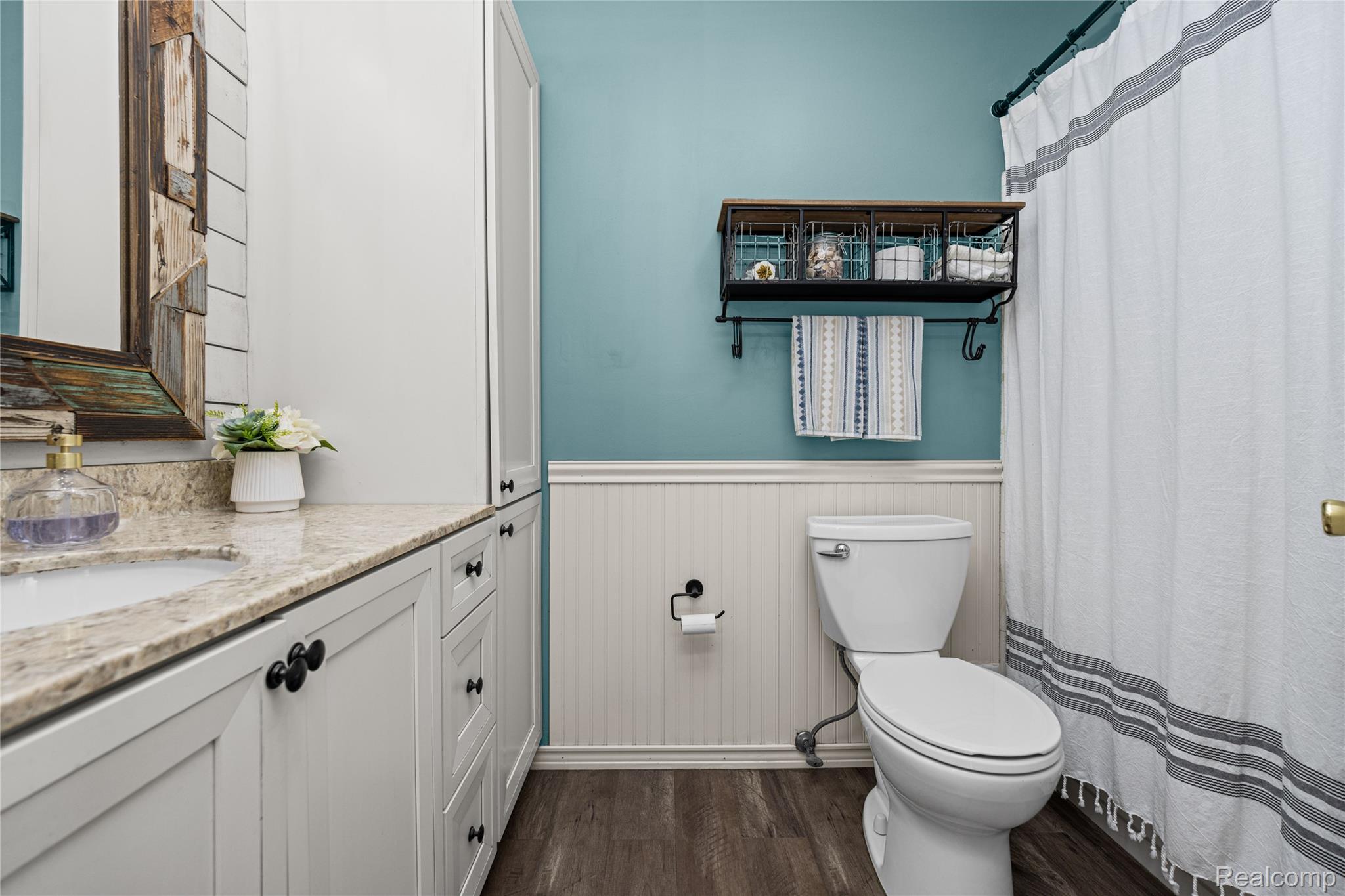 3553 Loon Lake Road Wixom, MI 48393 - Photo 15 of 25 Bathroom featuring a single vanity with a light-colored countertop, white cabinetry with black hardware, wood-finish flooring, white beadboard wainscoting, and a white toilet