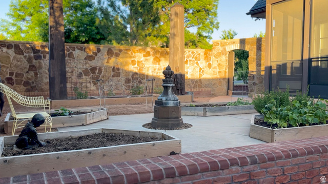 426 West Center Street Parowan, UT 84761 - Photo 88 of 107 Paved patio area featuring multiple raised wooden garden beds, a stone accent wall, and a brick knee wall