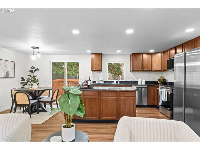 a kitchen with stainless steel appliances granite countertop a refrigerator a sink a stove a dining table and chairs with wooden floor