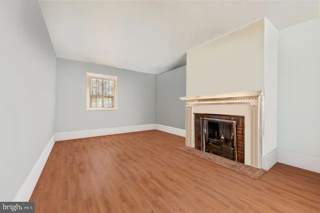 a view of an empty room with wooden floor fireplace and a window