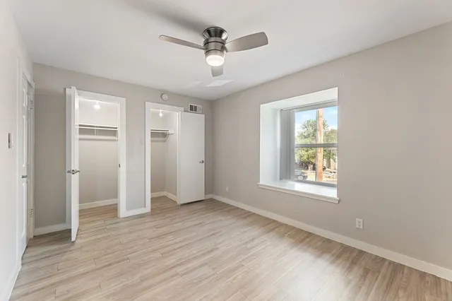 an empty room with wooden floor fan and windows