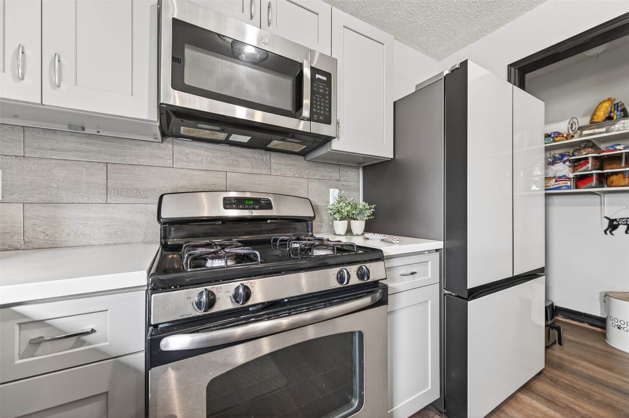 18446 North Willow Bluff Road Katy, TX 77449 - Photo 16 of 33 Modern kitchen with stainless steel appliances, including a gas stove and microwave. Sleek white cabinetry and a tiled backsplash complement the clean design. Spacious pantry visible to the right.