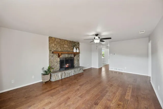a view of a livingroom with a fireplace a ceiling fan and wooden floor