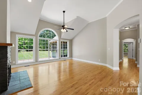a view of an empty room with wooden floor kitchen view and a window