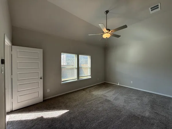 an empty room with chandelier fan and windows