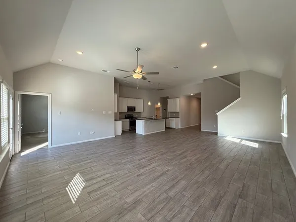 a view of an empty room and kitchen with wooden floor