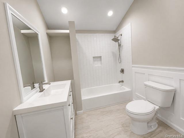 321 Sherbrooke Road Lindenhurst, NY 11757 - Photo 21 of 21 Modern bathroom featuring a white vanity with integrated sink, rectangular framed mirror, built-in tub with vertical tile surround, and wainscoting detail