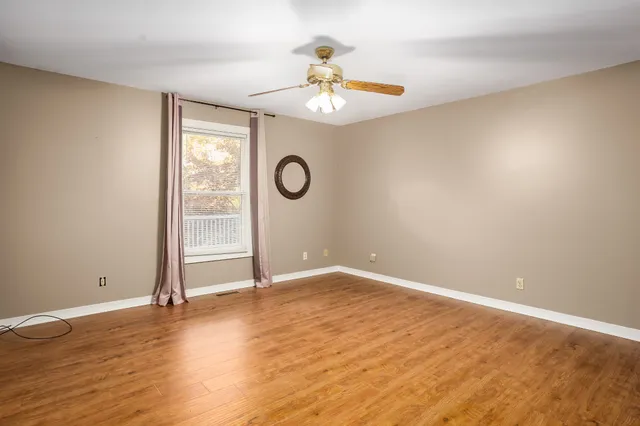 a view of an empty room with chandelier fan and wooden floor
