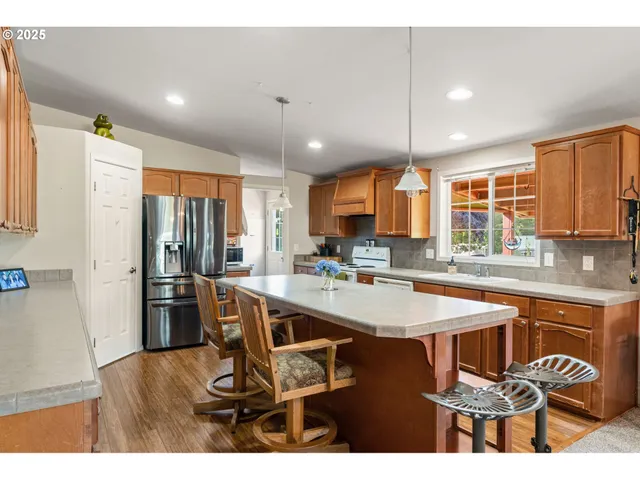 a kitchen with stainless steel appliances kitchen island granite countertop a refrigerator a sink a stove and white cabinets with wooden floor