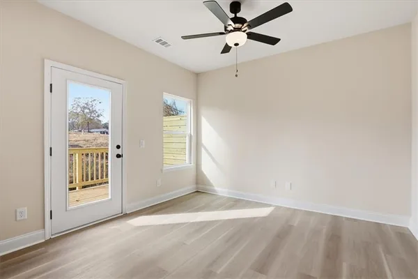 an empty room with wooden floor fan and windows