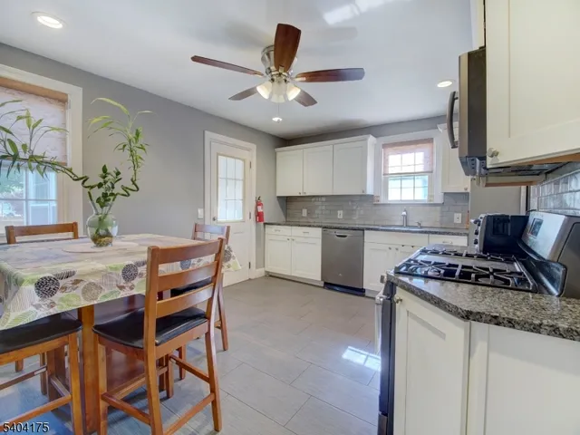 a kitchen with stainless steel appliances granite countertop a stove top oven a sink a dining table and chairs with wooden floor