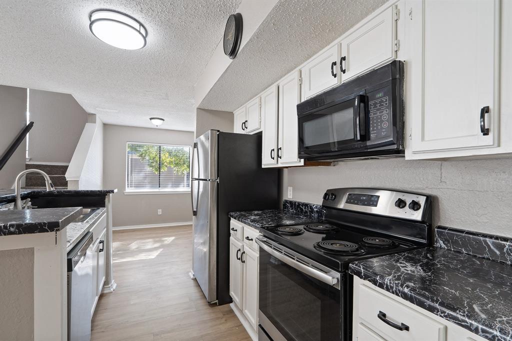9831 Walnut Street, Unit 205 Dallas, TX 75243 - Photo 11 of 29 Kitchen with a textured ceiling, stainless steel appliances, light hardwood / wood-style flooring, dark stone countertops, and white cabinets