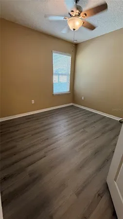 an empty room with wooden floor chandelier fan and windows