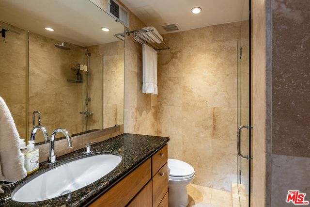 a bathroom with a granite countertop sink a toilet a mirror and shower