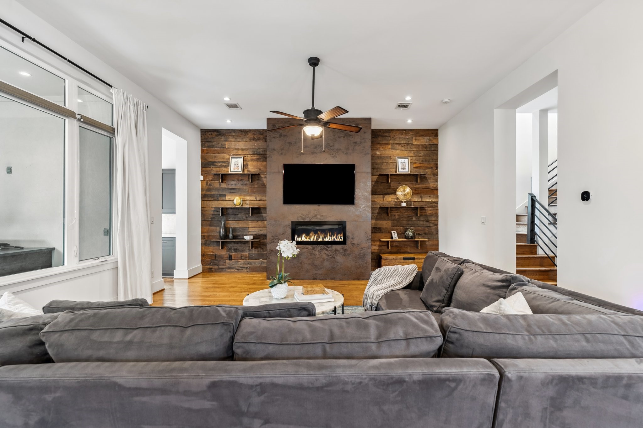 815 East 27th Street Houston, TX 77009 - Photo 44 of 44 The family room is the heart of this open floor plan. A striking gas fireplace takes center stage, framed by large, single-piece Italian tiles that stack all the way to the ceiling, creating a bold and modern focal point. Reclaimed wood-paneled accents on either side of the fireplace add warmth & character, while display shelves provide the perfect space to showcase décor. Convenient hallway on the left provides access to the mudroom and attached garage.