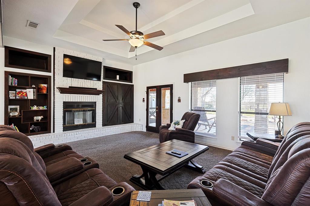 7185 Mesquite Ridge Sanger, TX 76266 - Photo 11 of 40 Carpeted living room featuring ceiling fan, a fireplace, a raised ceiling, and built in features