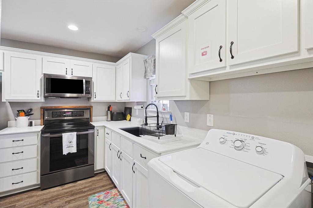 7185 Mesquite Ridge Sanger, TX 76266 - Photo 32 of 40 Kitchen featuring washer / clothes dryer, wood-type flooring, appliances with stainless steel finishes, and white cabinets