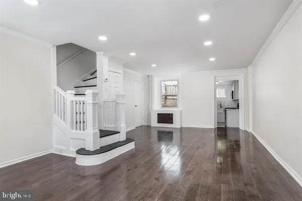 a view of an empty room with wooden floor and kitchen
