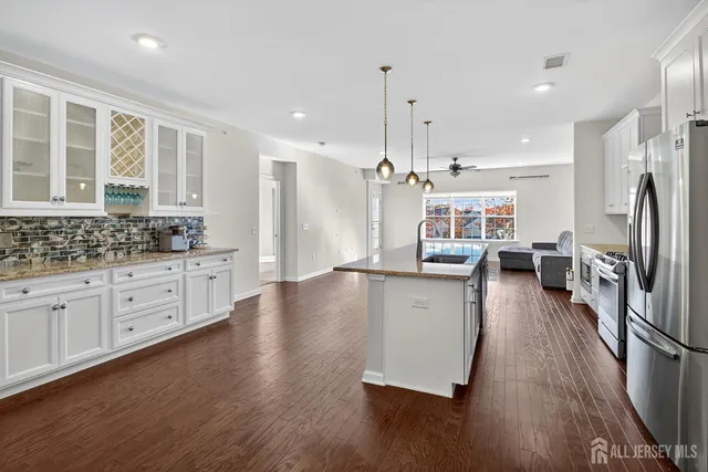 a kitchen with stainless steel appliances granite countertop a refrigerator a stove oven a sink dishwasher and white cabinets with wooden floor