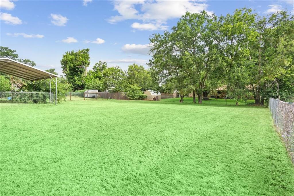 608 9th Street Hico, TX 76457 - Photo 20 of 23 Expansive green lawn featuring a metal carport structure, mature trees, and chain link fencing