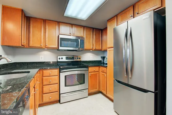a kitchen with stainless steel appliances granite countertop a refrigerator stove a sink and dishwasher with wooden cabinet