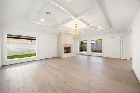 an empty room with wooden floor fireplace and chandelier