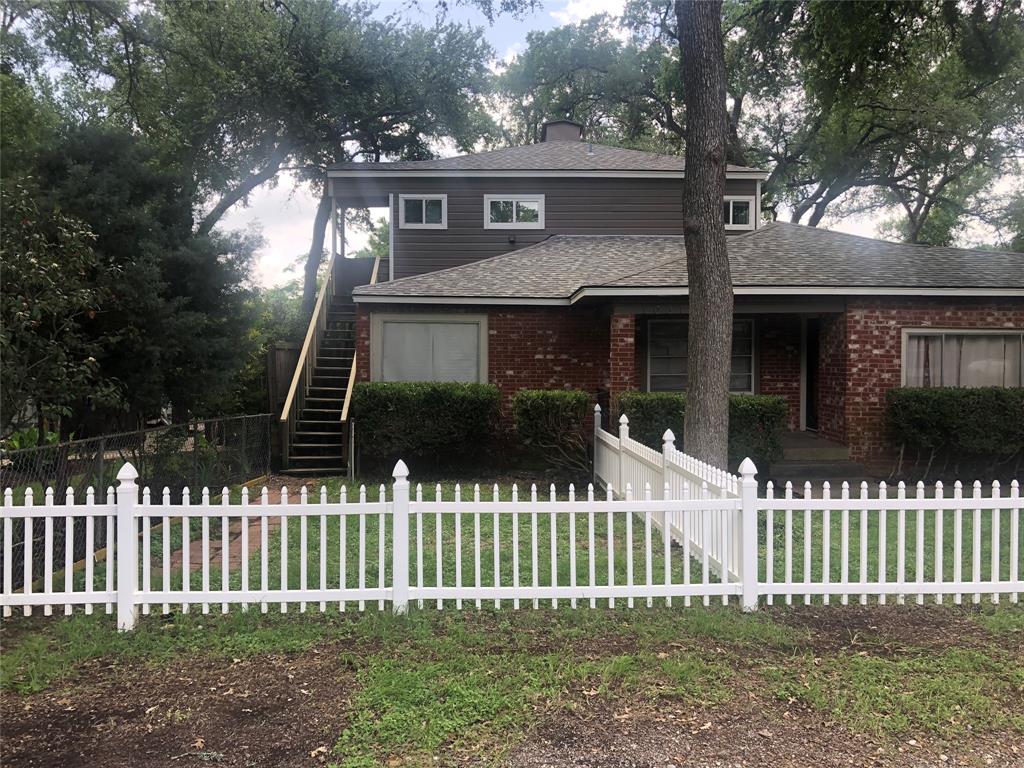 A charming brick residence features a picket fence and mature shade trees.
