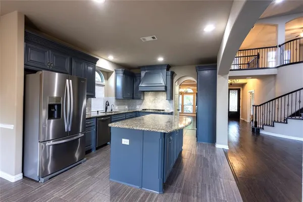 a kitchen with stainless steel appliances granite countertop a refrigerator a sink dishwasher a stove and a dining table with wooden floor