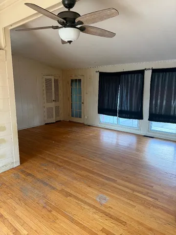 a view of an empty room with wooden floor and a ceiling fan