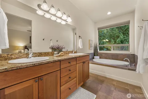 a bathroom with a granite countertop sink a large mirror and a bathtub next to a window