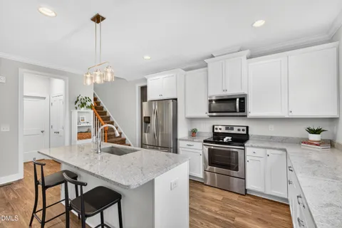 a kitchen with stainless steel appliances granite countertop a stove a sink dishwasher a refrigerator white cabinets and wooden floor