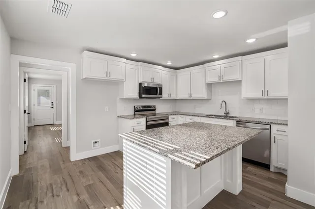 a kitchen with stainless steel appliances granite countertop a stove top oven a sink dishwasher and a refrigerator with wooden floor